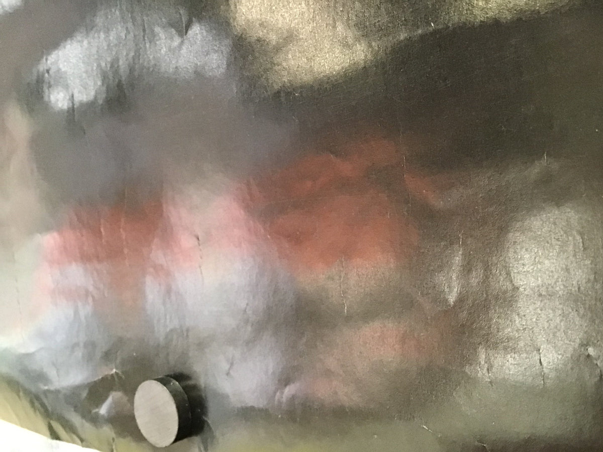 A close-up of a dark, metallic surface with a brushed or textured finish, showing gray, silver, and reddish-brown tones. A small circular metallic piece is visible near the lower left.