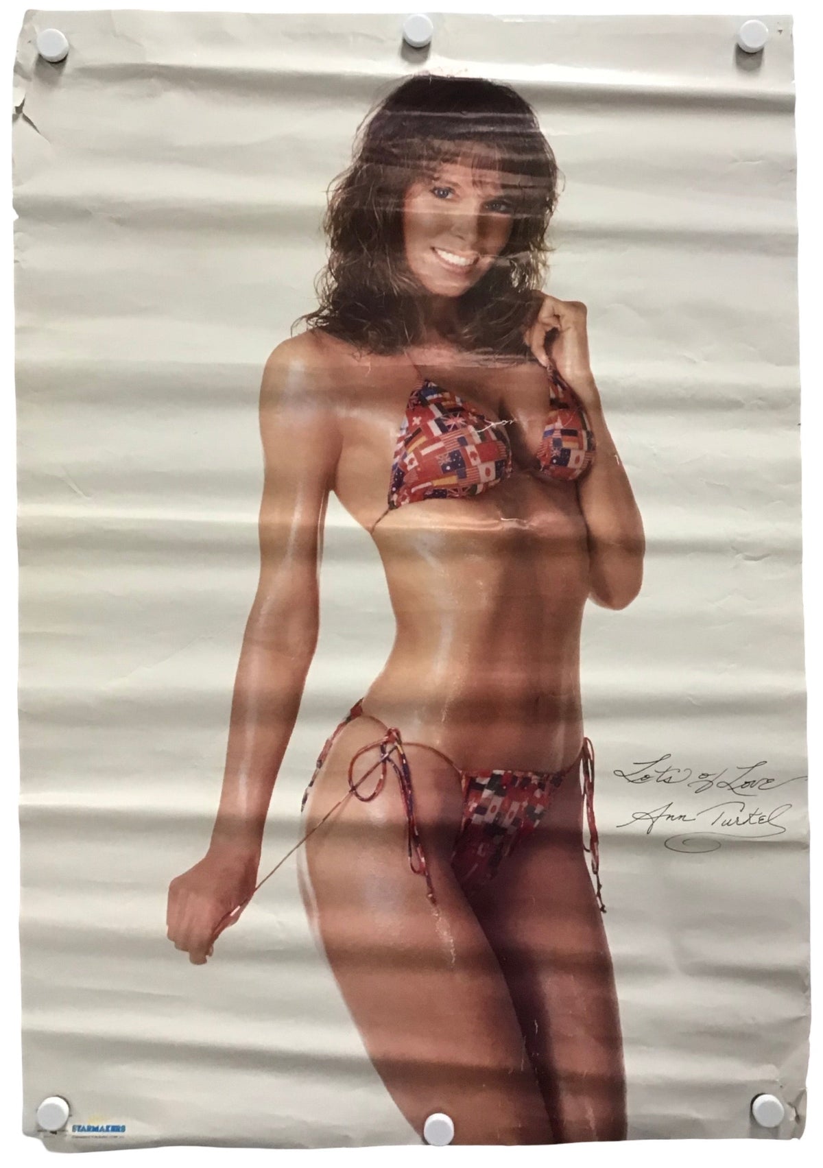 A vintage-style poster print featuring a woman in a red and blue patterned bikini, displayed flat with visible fold lines and white hanging clips at the corners.