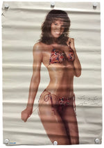 A vintage-style poster print featuring a woman in a red and blue patterned bikini, displayed flat with visible fold lines and white hanging clips at the corners.