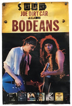 Vintage-style metal sign for Joe Dirt Car and Bodeans, featuring a yellow header with distressed text and a black-and-color photo of two men playing guitars, mounted against a white background.