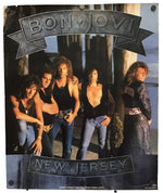 A vintage-style Bon Jovi poster featuring the band members standing outdoors near a pier or dock, with large 'BON JOVI' lettering at the top and 'NEW JERSEY' at the bottom. The poster is photographed hanging against a plain light background.
