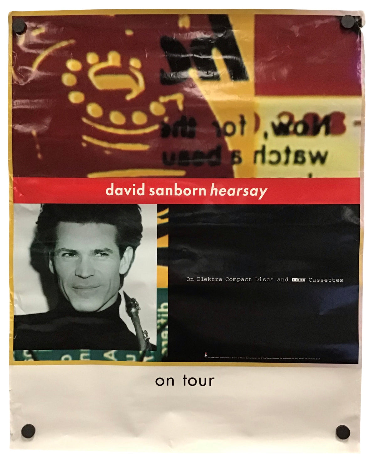 A vintage concert poster for David Sanborn 'Hearsay' on tour, featuring a collage design with a portrait, a red banner, and a black background, displayed on a white sheet with binder clips.