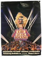 Vintage movie soundtrack poster for 'The Day of the Locust' on a plain white background. The poster features a blonde woman with dramatic makeup, a crowd of people at the bottom, and white spotlights radiating from the top against a dark background.