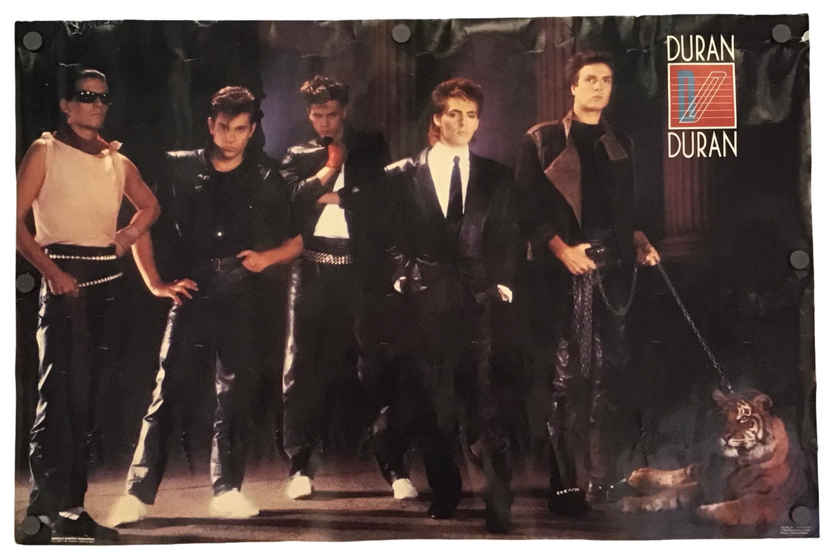 A rectangular Duran Duran band poster featuring a group photo of the five members in dark outfits, with the Duran Duran logo in the top right corner, shown against a plain white background.