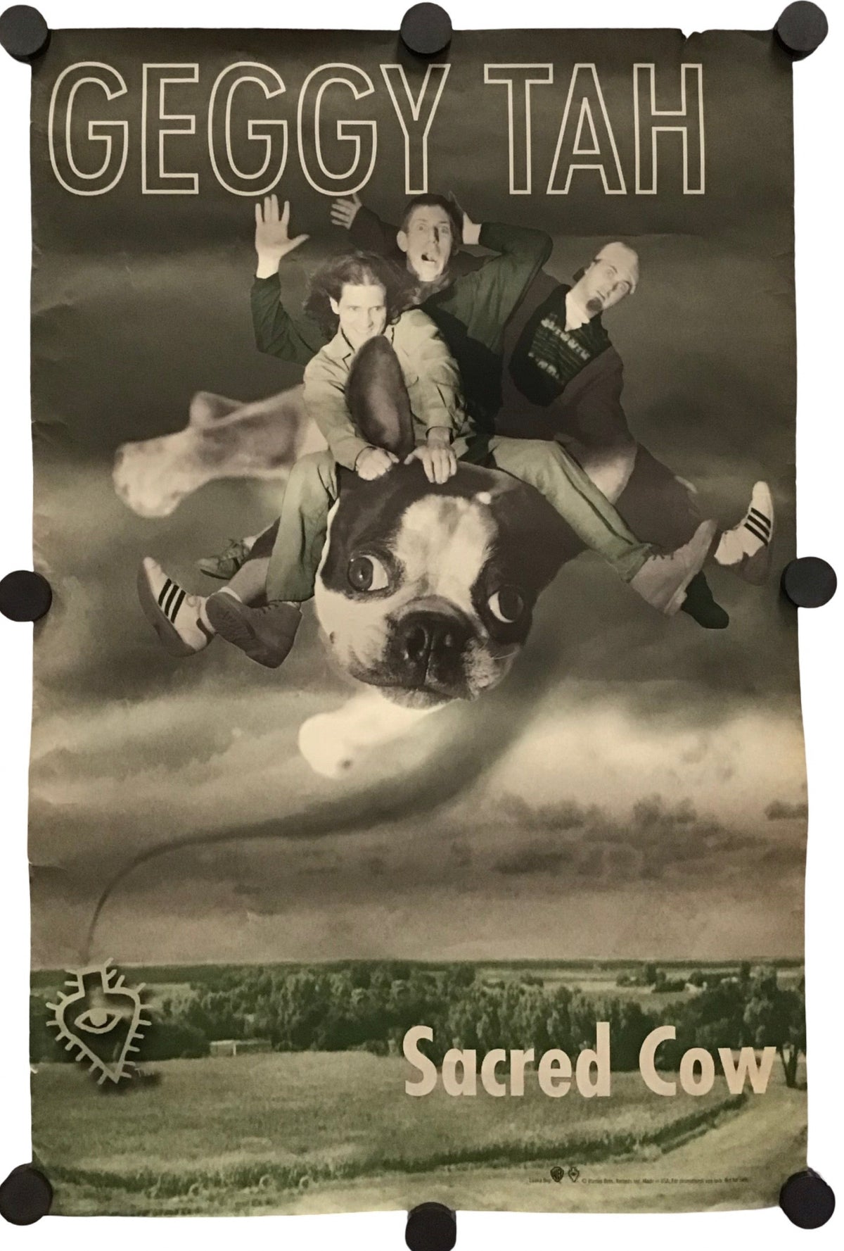 A rectangular wall banner or flag with black corner and edge clips, featuring a sepia-toned surreal photo of three people riding a dog against a cloudy sky, with the text 'GEGGY TAH' at the top and 'Sacred Cow' at the bottom.