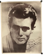 A vintage black and white portrait photograph print of a young man, signed in cursive script in the lower right corner, displayed with black binder clips at the corners.