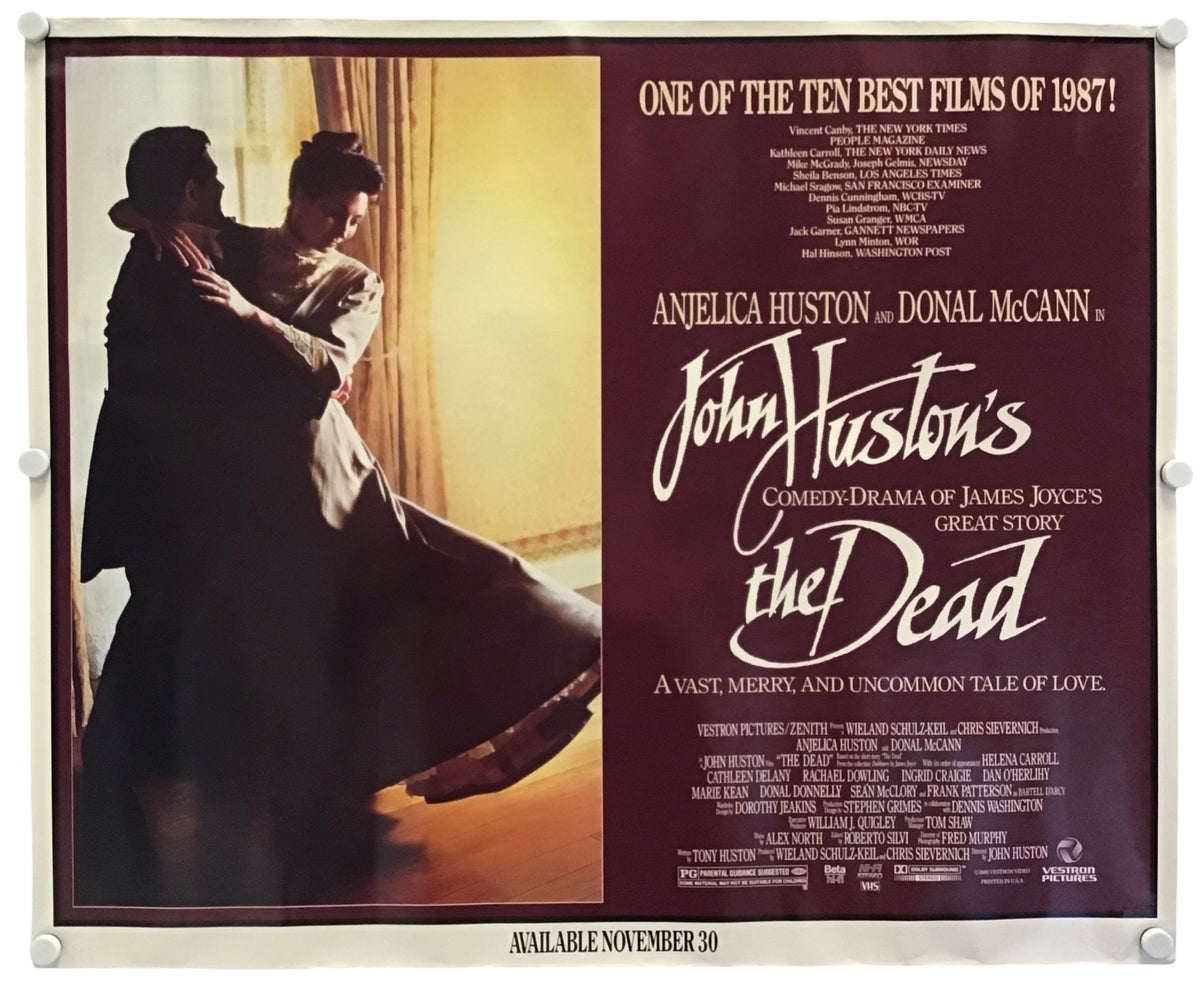 A vintage movie poster for 'John Huston's The Dead' hangs against a white wall, secured with small clips at the corners. The poster features a split design: a warm-toned photograph on the left showing a couple embracing, and a dark reddish-brown text panel on the right with white title lettering and film details.
