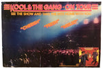 A vintage concert poster for Kool & The Gang's 'On Tour' tour, featuring a crowd scene under stage lights with the band's name in red at the top and song titles 'Cherish', 'Fresh', and 'Misled' in orange.