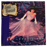 A square album cover for Linda Ronstadt's 'What's New' featuring a ballerina in a pink tutu against a dark purple draped background, with a gold-bordered title label on the left.