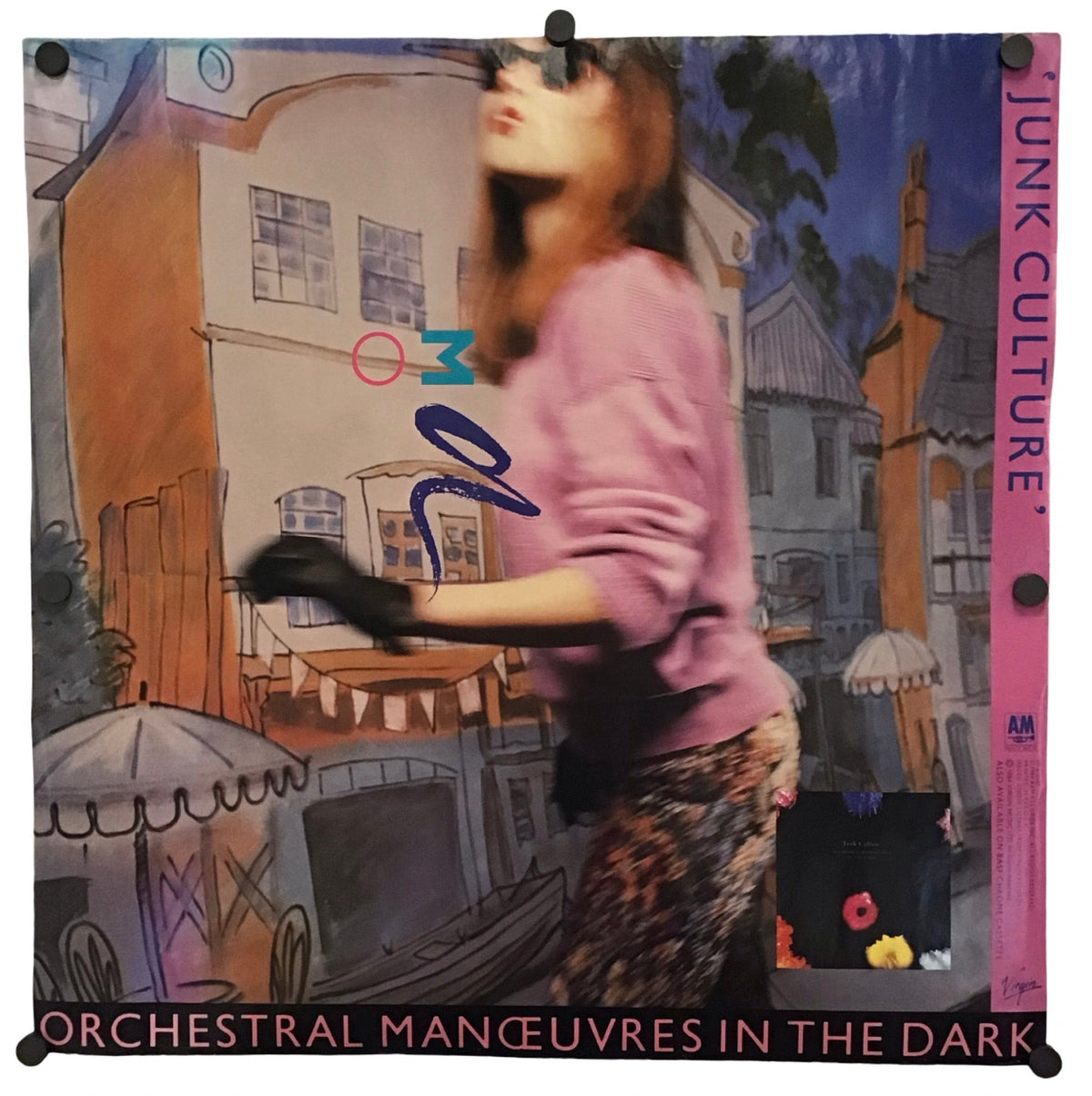 A square fabric banner or poster featuring a stylized illustration of a woman in a pink top and patterned skirt on a street scene, with the text 'ORCHESTRAL MANÈUVRES IN THE DARK' at the bottom and 'JUNK CULTURE' on the right edge. The banner is displayed against a plain white background with clips at the corners.
