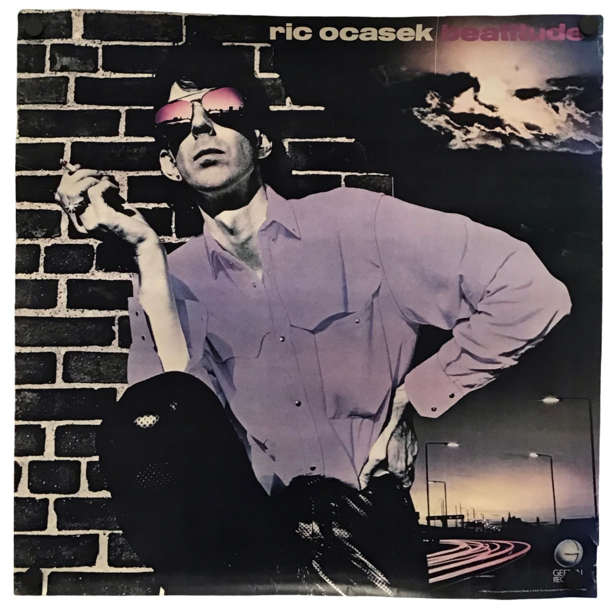 A square album cover for 'Anomalous' by Ric Ocasek, featuring a stylized portrait of a man in a lavender shirt and pink sunglasses against a brick wall and dark night sky.