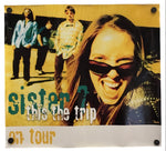 A rectangular printed poster or banner with four metal grommets in the corners, featuring a band photo and the text 'sister 7 this the trip on tour'.