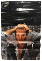 A vertical poster or print featuring a stylized portrait of a man with his hands on his head, overlaid with a cracked black texture and the word 'STAGE' in white at the top. The print is shown hanging against a white wall.
