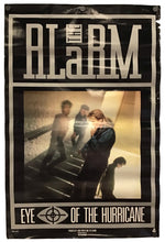 A vintage-style band poster for the band Alarm, featuring the album title 'Eye of the Hurricane' and a central photograph of members standing on stairs, shown against a plain white background.