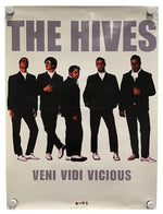A vintage-style band poster for 'The Hives' featuring five men in black suits against a light background, with the text 'THE HIVES' at the top and 'VENI VIDI VICIOUS' at the bottom. The poster is shown hanging with visible wall fasteners.