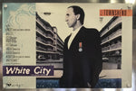 A vintage album cover for Pete Townshend's 'White City' mounted on a metallic wall. The cover features a black-and-white portrait of a man in a suit, modernist architectural buildings, and a light blue textured background on the left side.