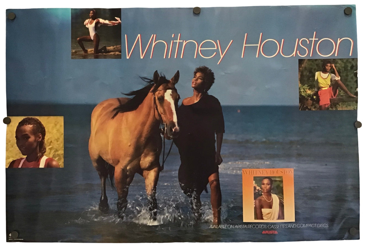 A Whitney Houston poster or print featuring a large photo of her standing in shallow water beside a horse, with smaller inset photos and the text 'Whitney Houston' across the top. The poster is photographed against a plain white background.