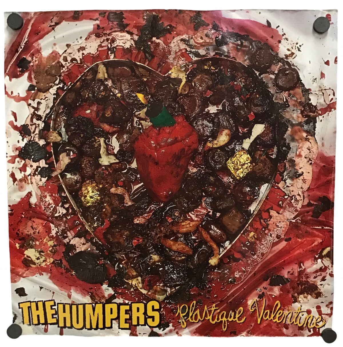 A square art print or poster featuring a stylized chocolate heart with a red heart-shaped pepper in the center, surrounded by red and white paint-like splatters. The bottom has yellow text reading 'THE HUMPERS' and 'Plastique Valentine'.