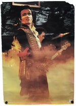 A square art print or poster featuring a stylized portrait of Adam Ant on stage, with a guitar and dramatic warm lighting, shown against a white background with visible mounting holes in the corners.