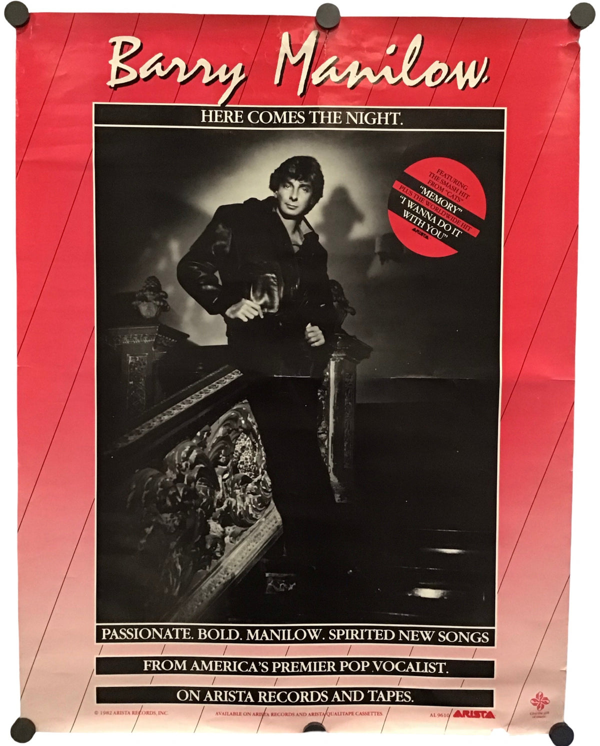 A vintage Barry Manilow promo poster mounted on a white wall with black binder clips at the corners. The poster features a red border, a black-and-white photo of the artist, and text including 'Barry Manilow' and 'Here Comes the Night'.