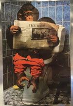 A square photographic print or poster mounted on a metallic wall, showing a chimpanzee sitting on a toilet in a tiled bathroom and reading a newspaper titled THE TIMES.