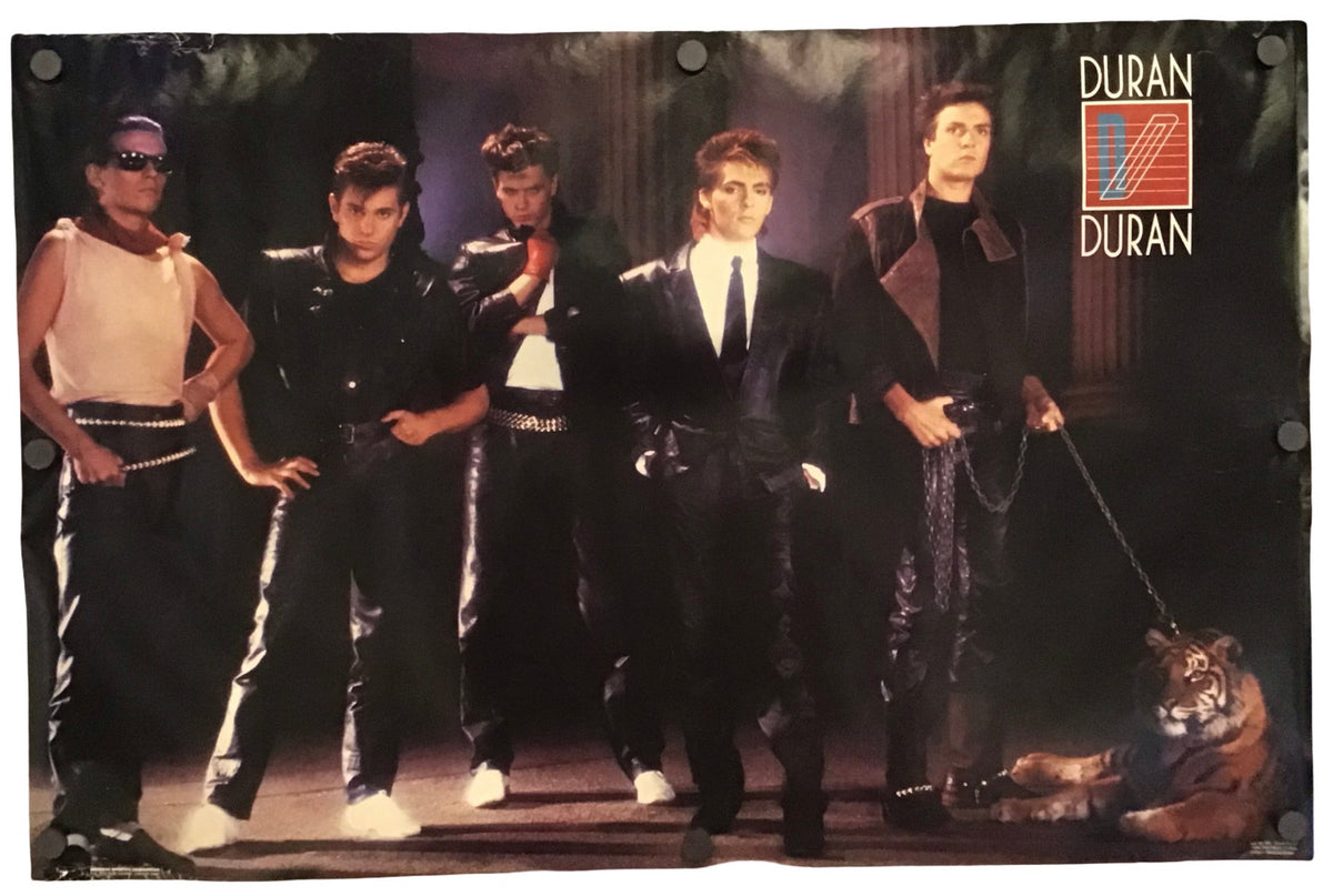 A vintage Duran Duran band poster featuring the five members in black outfits, with a tiger on a leash at the bottom right and the 'Duran Duran' logo in the top right corner, displayed against a white background.