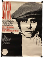 A vintage-style Elton John poster print hanging against a white wall, with black binder clips at the corners. The poster features a large black-and-white portrait of Elton John wearing a flat cap, with red and black text including 'ELTON JOHN' and 'The Zion Bell Sessions.