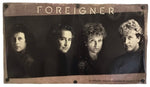A rectangular wall plaque featuring a sepia-toned band photo of Foreigner with the band name printed in gold at the top, mounted on a white background.