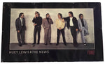 A vintage band poster for 'Huey Lewis & The News - Fore!' featuring a black border with a color photograph of the band members standing against a textured wall.