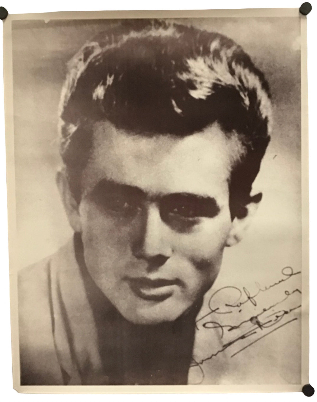 A vintage black and white portrait photograph print of a young man, signed in cursive script in the lower right corner, displayed with black binder clips at the corners.