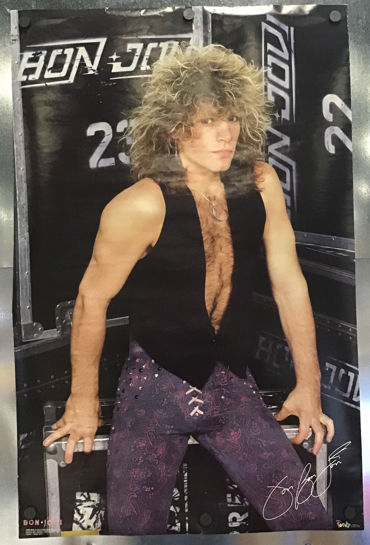 A poster of Jon Bon Jovi featuring him in a black vest and purple pants, displayed on a metallic surface.