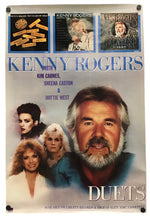 A vintage Kenny Rogers 'Duets' album poster print featuring a large portrait of Kenny Rogers, smaller portraits of Kim Carnes, Sheena Easton, and Dottie West, and three album cover thumbnails at the top. The poster is photographed hanging against a plain light background.