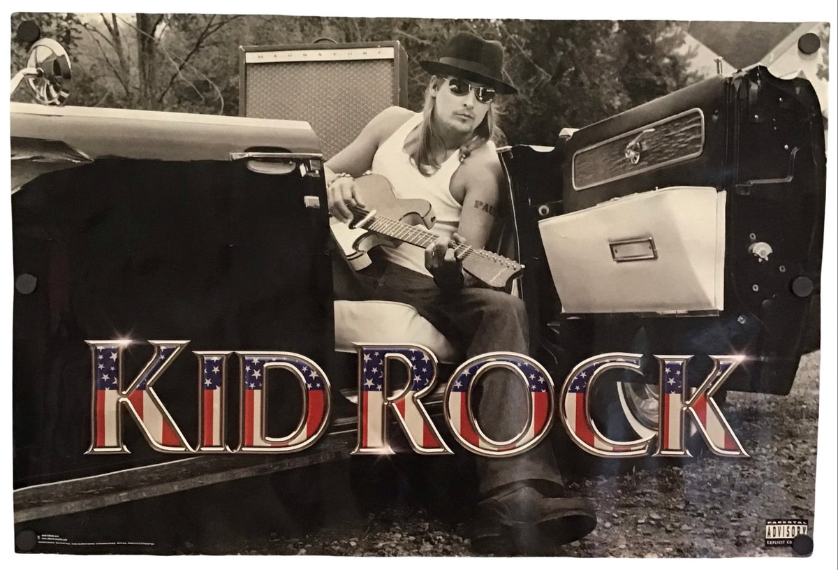 A rectangular music poster for the band Kid Rock, featuring a black-and-white photo of a man in a hat sitting in the back of a truck and holding a guitar, with the text 'KID ROCK' in large patriotic red, white, and blue lettering across the bottom.