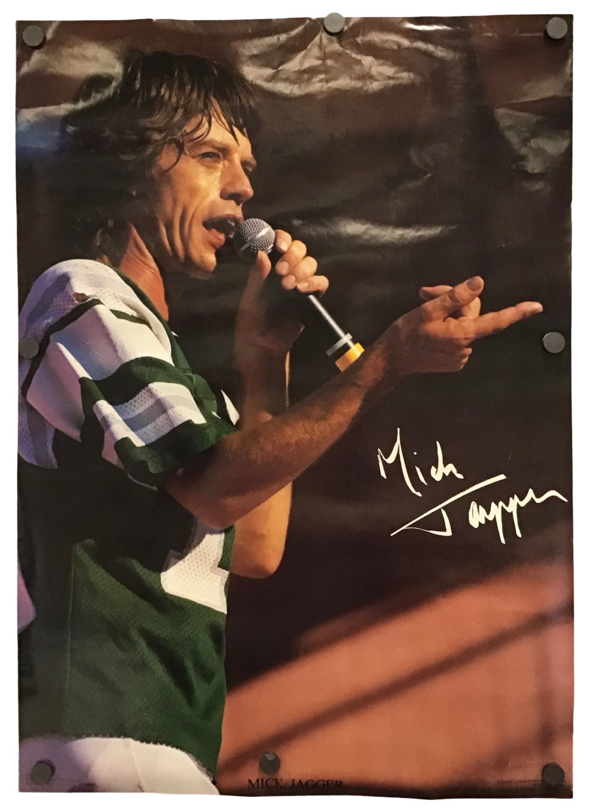 A photo print of Mick Jagger performing live, his signature in white print, displayed on a white background with visible mounting holes and clips.