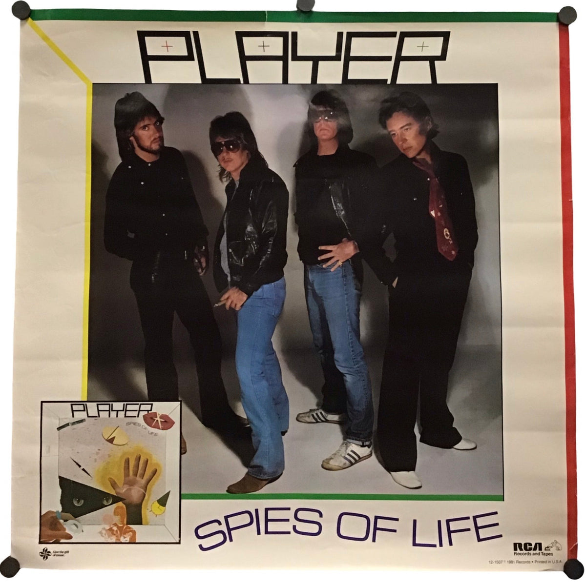 A vintage music poster for the band Player, titled 'Spies of Life', featuring a group photo of the four band members and album artwork in the bottom-left corner, displayed on a white background with black binder clips at the corners.