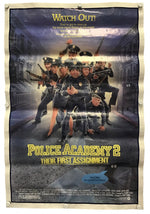 A vintage-style movie poster for 'Police Academy 2: Their First Assignment' displayed flat against a light background, secured with small pins at the corners.