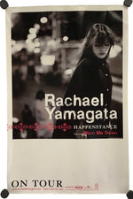 A vertical concert poster for Rachael Yamagata's 'Happenstance' tour, featuring a black and white photograph of the artist, with red and white text, displayed on a white background with black mounting clips at the corners.