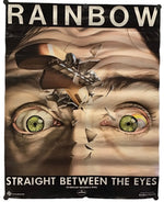 A poster print featuring a surreal close-up of a face with green eyes, broken shards, and a small airplane, with the text 'RAINBOW' at the top and 'STRAIGHT BETWEEN THE EYES' at the bottom.