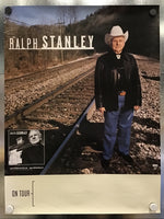 A printed Ralph Stanley on tour poster mounted on a metallic wall. The poster features a photo of Ralph Stanley standing on railroad tracks, with the text 'RALPH STANLEY' at the top and 'ON TOUR' on a cream-colored lower section.