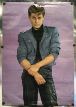 A vertical poster or print featuring a man in a blue jacket and dark pants against a lavender-purple background, displayed with black binder clips on a metallic surface.