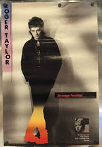 A Roger Taylor 'Strange Frontier' music poster mounted on a metallic wall. The poster features a black-and-white portrait of Roger Taylor with a stylized flame graphic in red, orange, and yellow at the bottom, alongside text including 'ROGER TAYLOR' and 'Strange Frontier'.