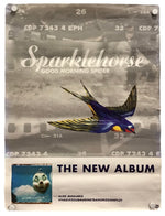 A rectangular printed poster or album cover artwork hanging against a white wall, with visible wall hooks at the corners. The design has a gray smoky background with the text 'Sparklehorse' and 'Good Morning Spider,' a large blue-and-yellow bird in flight across the center, and 'THE NEW ALBUM' near the bottom.