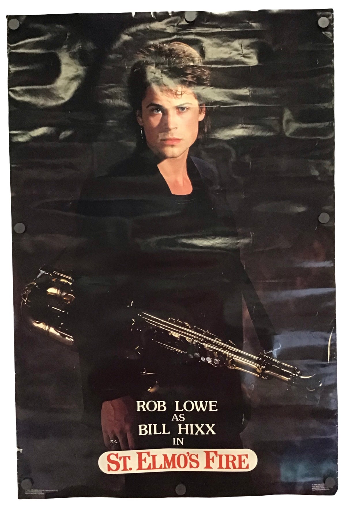 A vintage movie poster for the film 'St. Elmo's Fire' featuring Rob Lowe as Bill Hixx, shown hanging against a white wall.