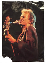 A vertical rectangular wall banner or poster featuring a photo print of a female singer performing live on stage, holding a microphone and guitar, with visible grommets along the top and left edges, set against a plain white background.