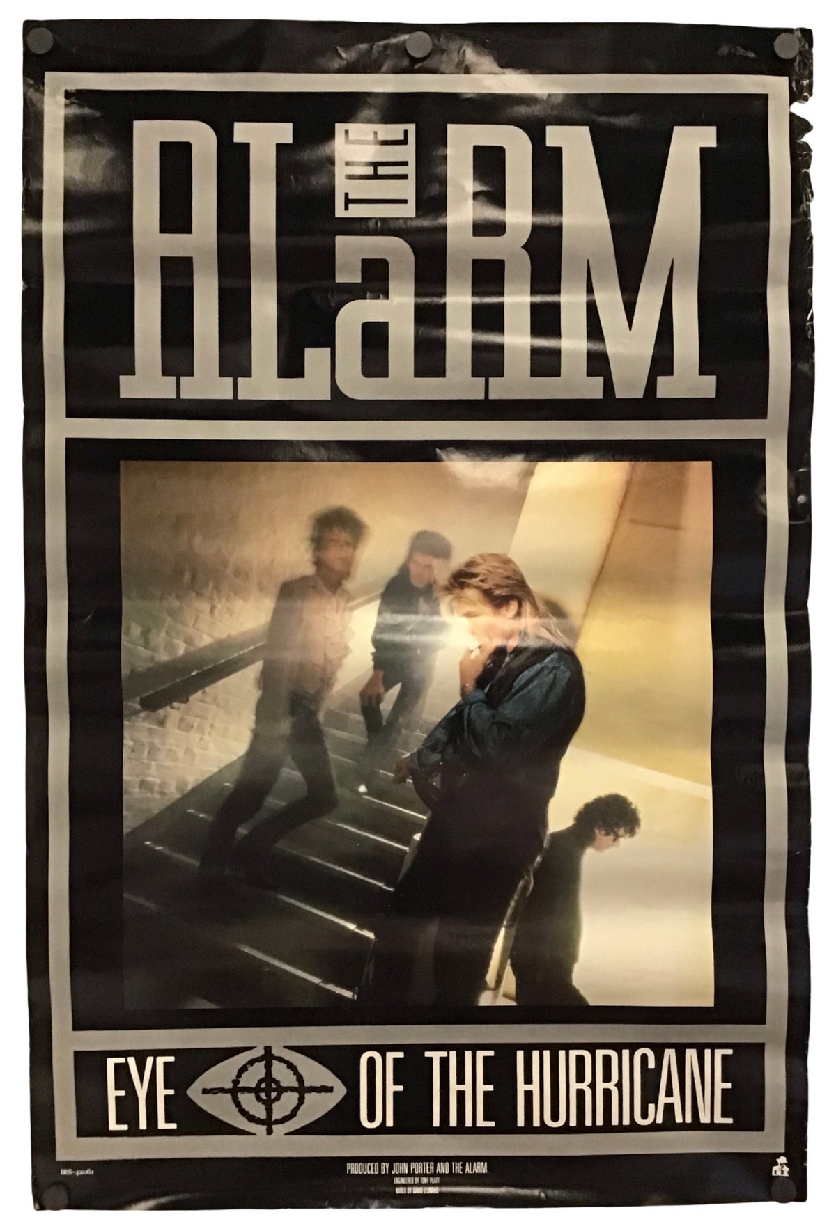 A vintage-style band poster for the band Alarm, featuring the album title 'Eye of the Hurricane' and a central photograph of members standing on stairs, shown against a plain white background.