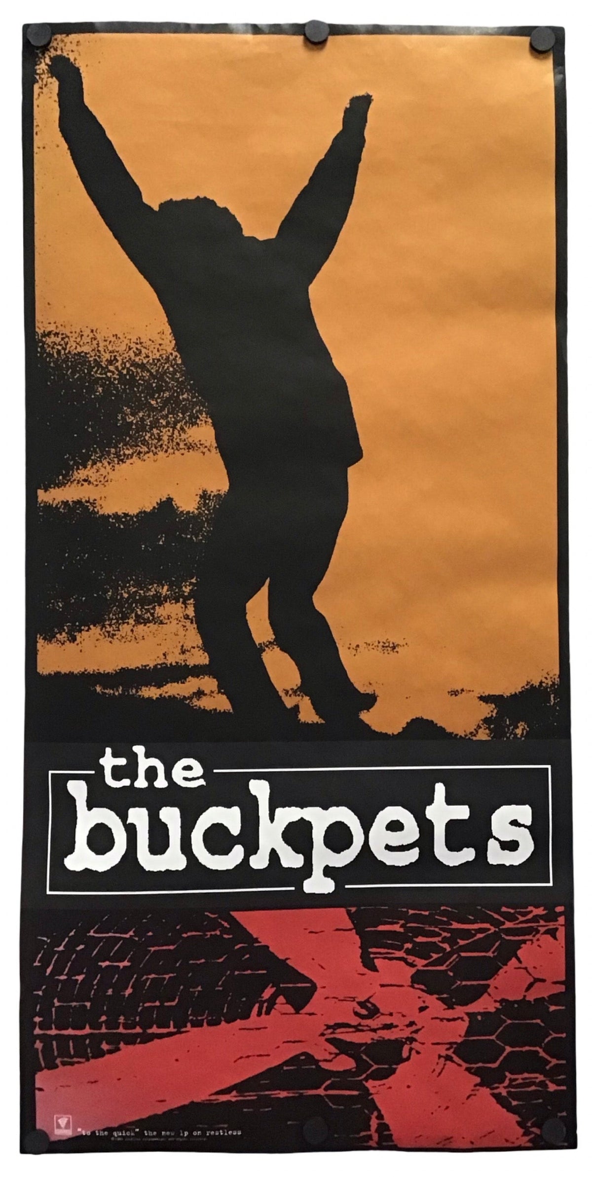 A vintage-style poster or print featuring a black silhouette of a person with raised arms against an orange-brown background, with the text 'the bucket' in white and a red abstract graphic at the bottom. The poster is shown hanging against a plain white wall.