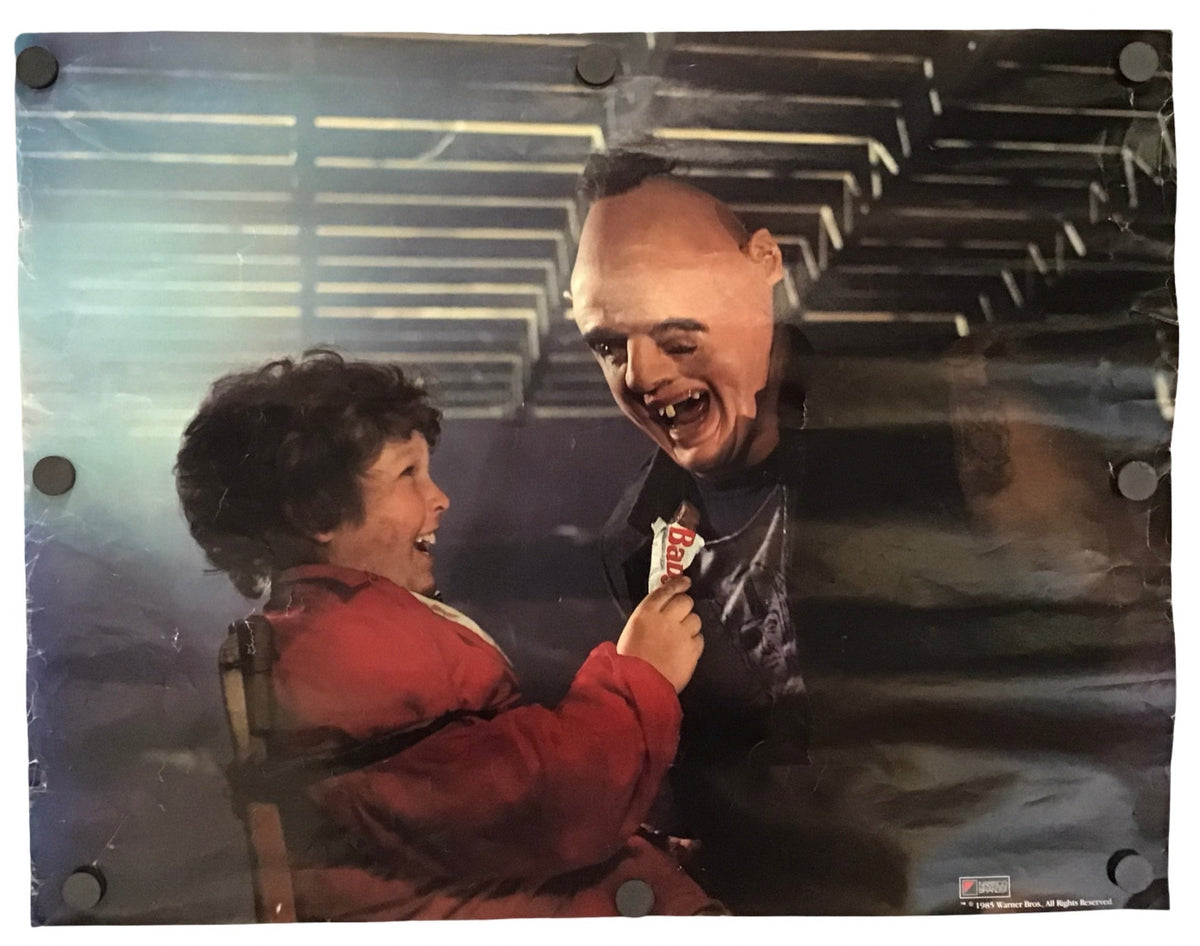 A rectangular printed artwork or poster showing a smiling bald man in a black leather jacket holding a small red-and-white object, with a child in a red jacket reaching toward him. The print is photographed against a plain white background and appears to be mounted or photographed flat with visible round fasteners along the left edge.
