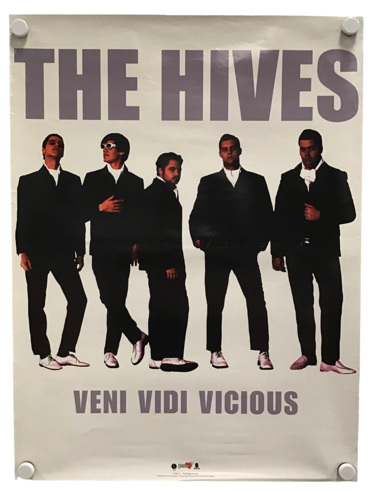 A vintage-style band poster for 'The Hives' featuring five men in black suits against a light background, with the text 'THE HIVES' at the top and 'VENI VIDI VICIOUS' at the bottom. The poster is shown hanging with visible wall fasteners.