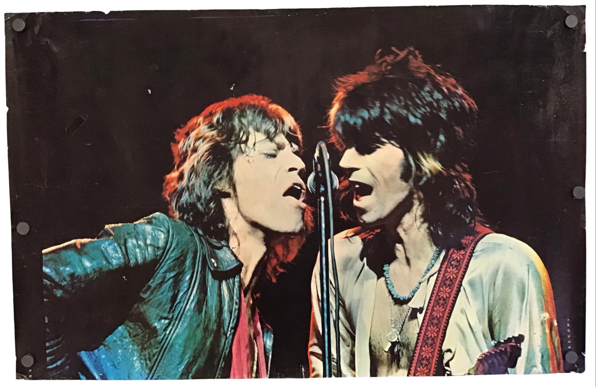 A vintage-style concert poster print depicting two rock musicians singing into microphones against a dark stage background, shown hanging with visible wall anchors on a white wall.