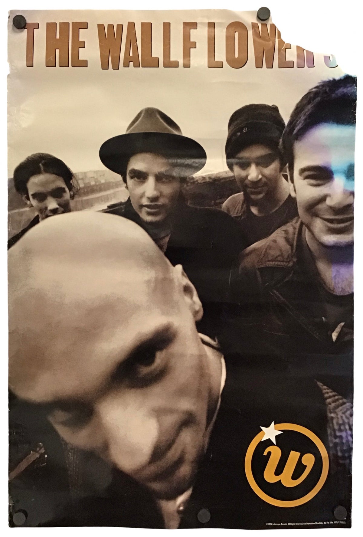 A vintage-style band poster for 'The Wallflowers' featuring a sepia-toned group portrait with a large close-up face in the foreground and a yellow circular 'w' logo near the bottom right, shown hanging against a white background.